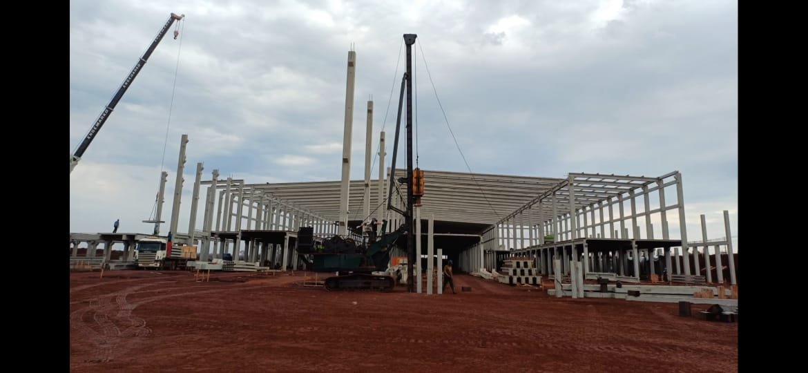 Canteiro de obras com equipamento de cravação de estacas sobre esteira operando entre estruturas pré-moldadas de concreto